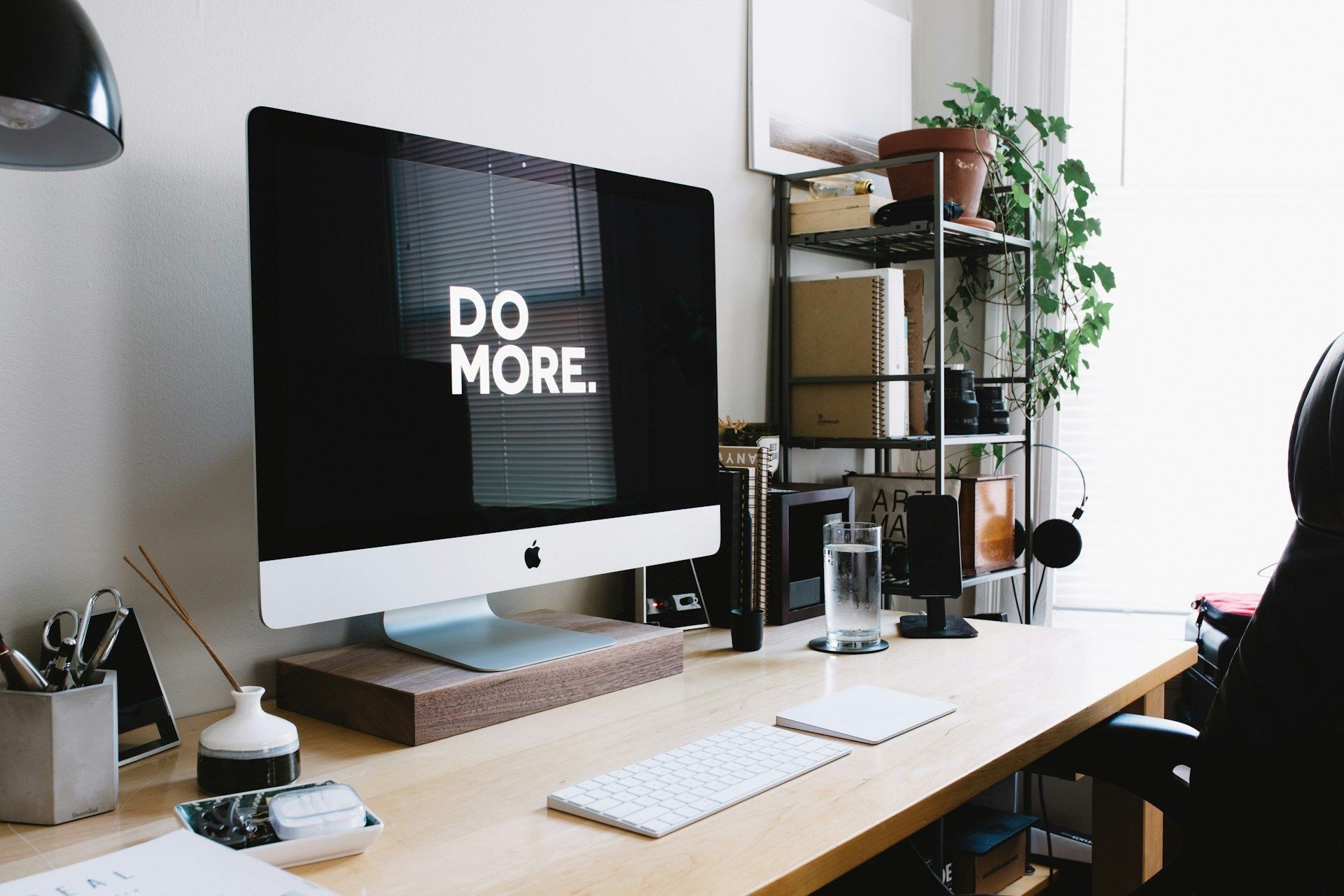 Creative workspace with a computer displaying 'Do More' and desk accessories, including plants and books.